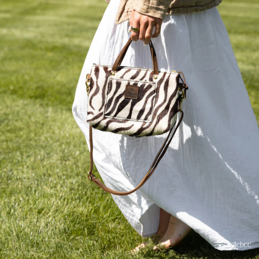 image of woman holding purse walking in a grass field and wearing a white dress