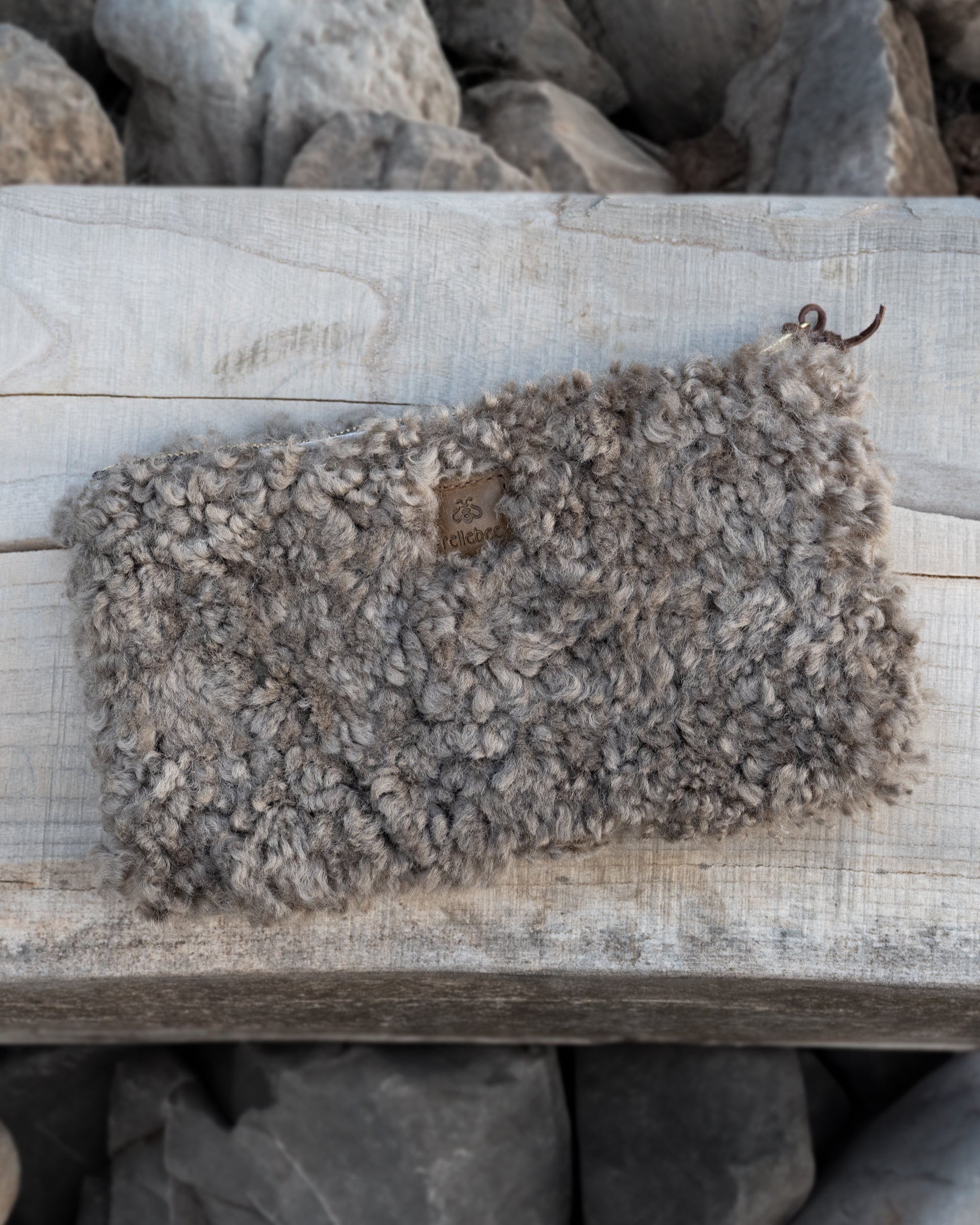 Image of the product the clutch in shearling placed on a wooden top