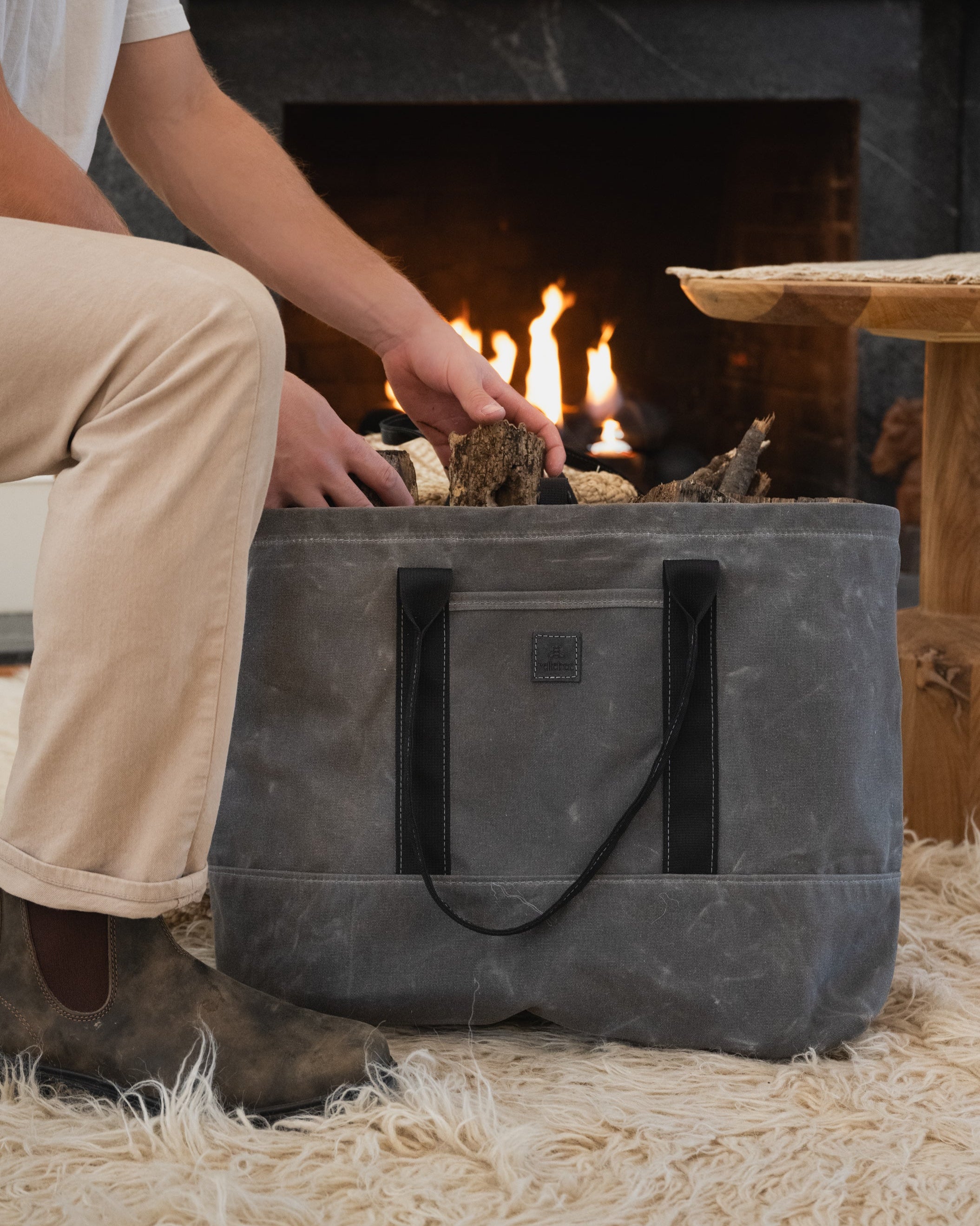 Image of model sitting and grabbing fire wood out of the utility tote in charcoal waxed