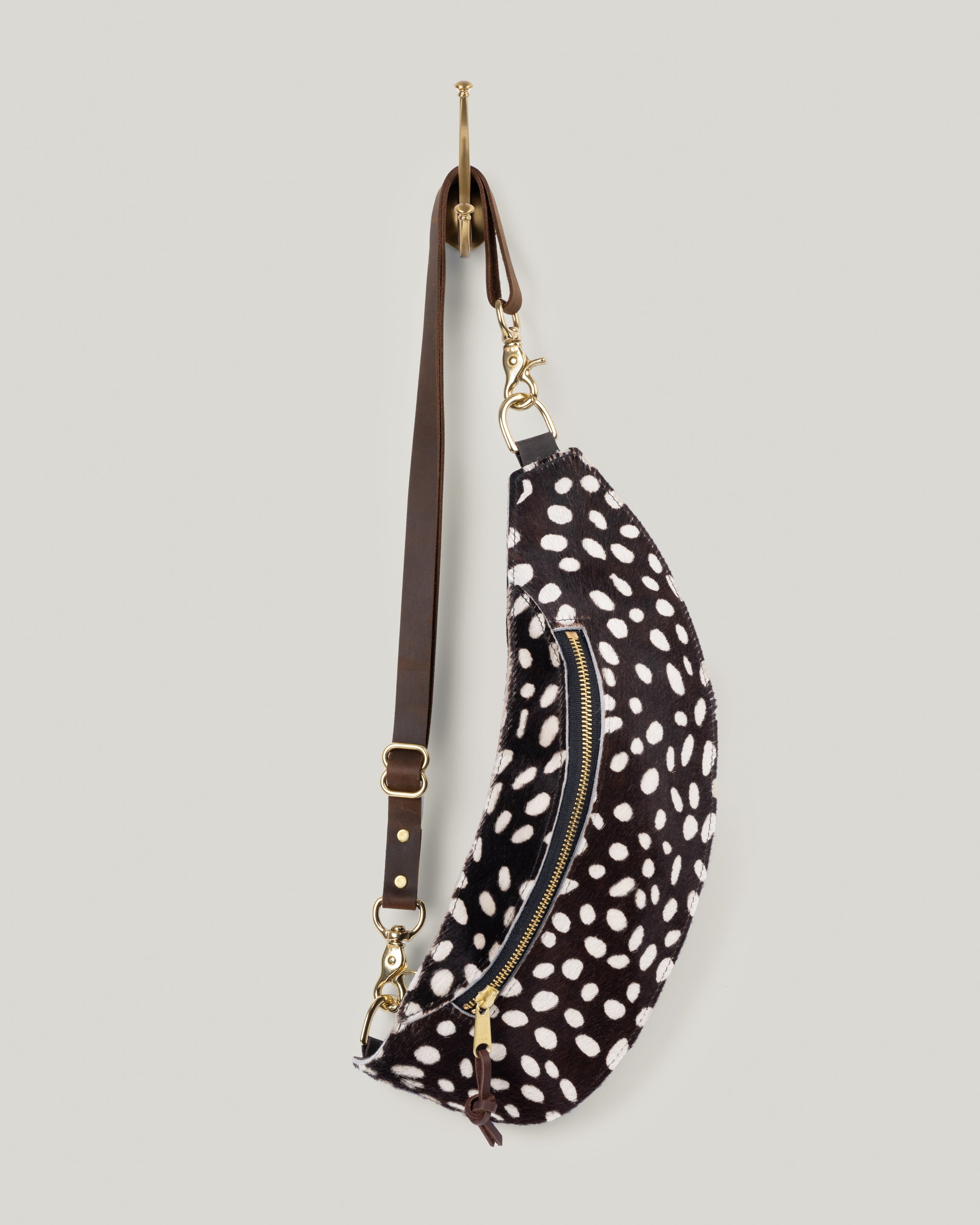 Image of the Classic Sling: Hair-on-hide in coco-dot: low profile and gently hugs your body. Just big enough to hold your phone, keys, mini wallet and chapstick. Adjustable bridle leather straps. Sturdy top of the line antique brass hardware and zipper. This Guernsey Hair-on-Hide collection gives the Classic Sling an extra level of playfulness and fun.
