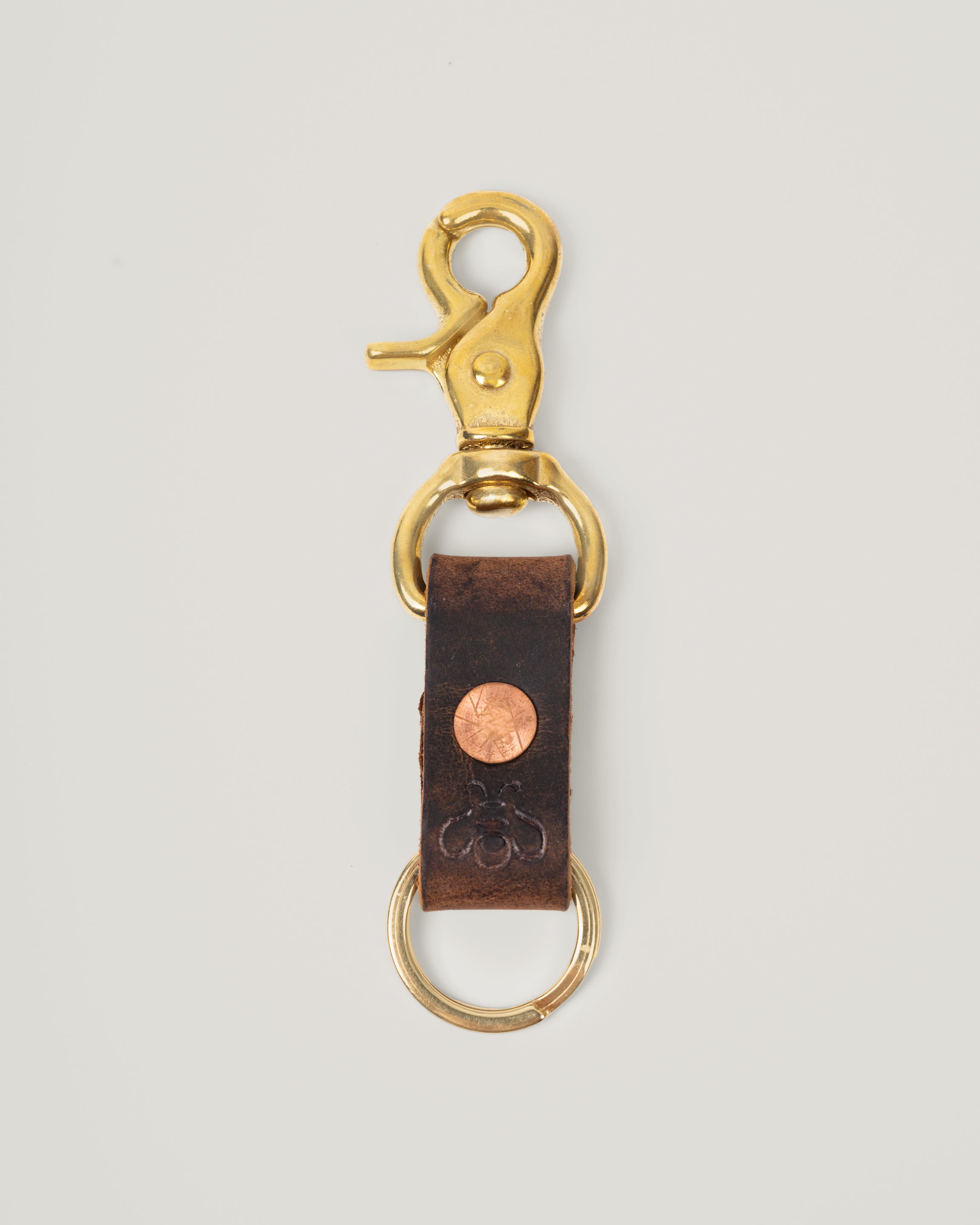 Image of product Brass Key Ring in Crazy Horse Brown: This rugged little key ring is made from a strip of full grain leather. The sturdy brass swivel snap hook is perfect to clip onto your sling, bag or jeans. Copper rivet gives an added pop and of course a small subtle branded bee.