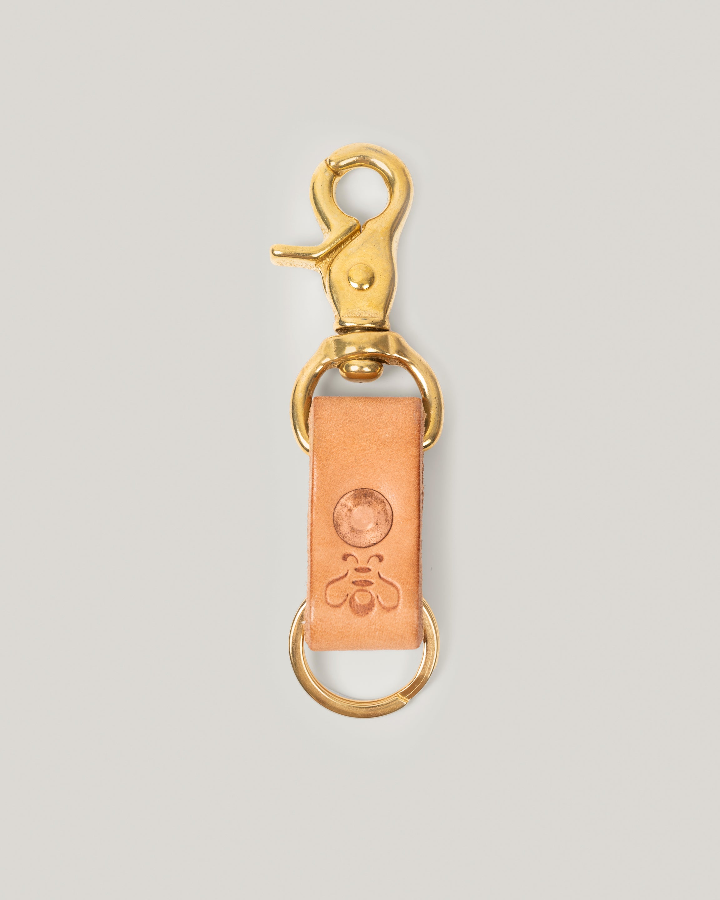 Image of product Brass Key Ring in Honey:This rugged little key ring is made from a strip of full grain leather. The sturdy brass swivel snap hook is perfect to clip onto your sling, bag or jeans. Copper rivet gives an added pop and of course a small subtle branded bee.