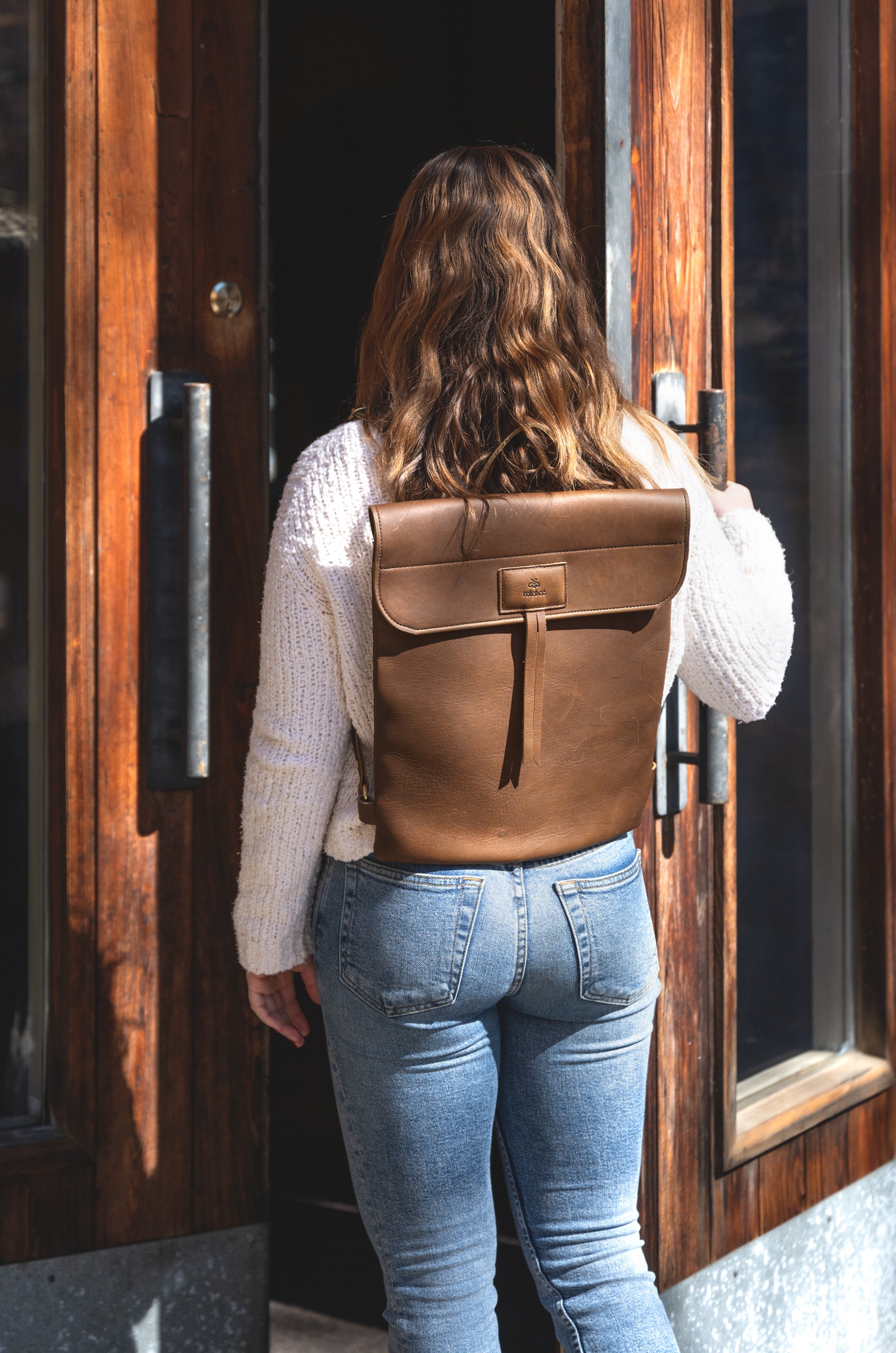 Back view image of model wearing the Messenger Pack in Olive Brown