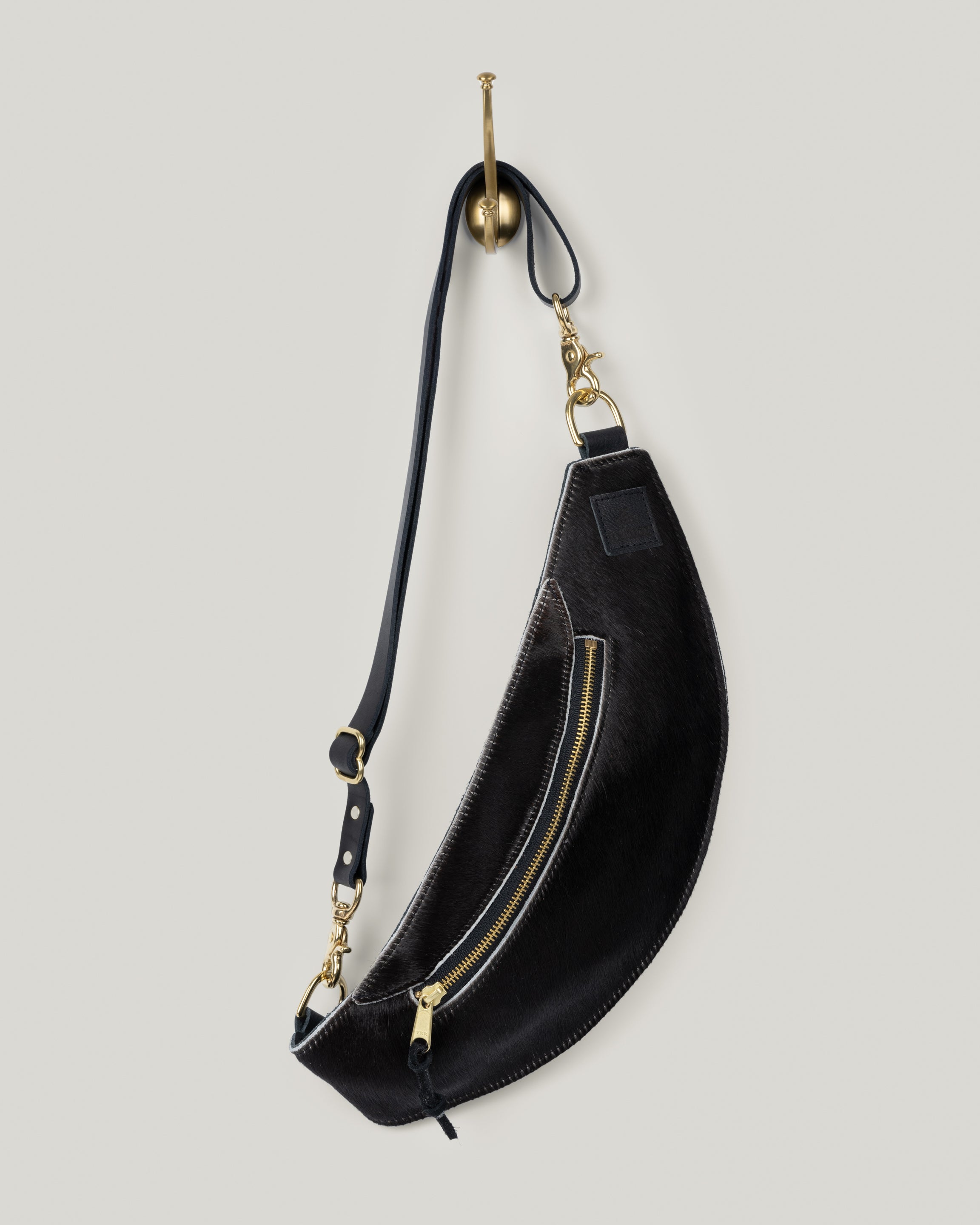 Image of the Classic Sling: Hair-on-hide in black: low profile and gently hugs your body. Just big enough to hold your phone, keys, mini wallet and chapstick. Adjustable bridle leather straps. Sturdy top of the line antique brass hardware and zipper. This Guernsey Hair-on-Hide collection gives the Classic Sling an extra level of playfulness and fun.