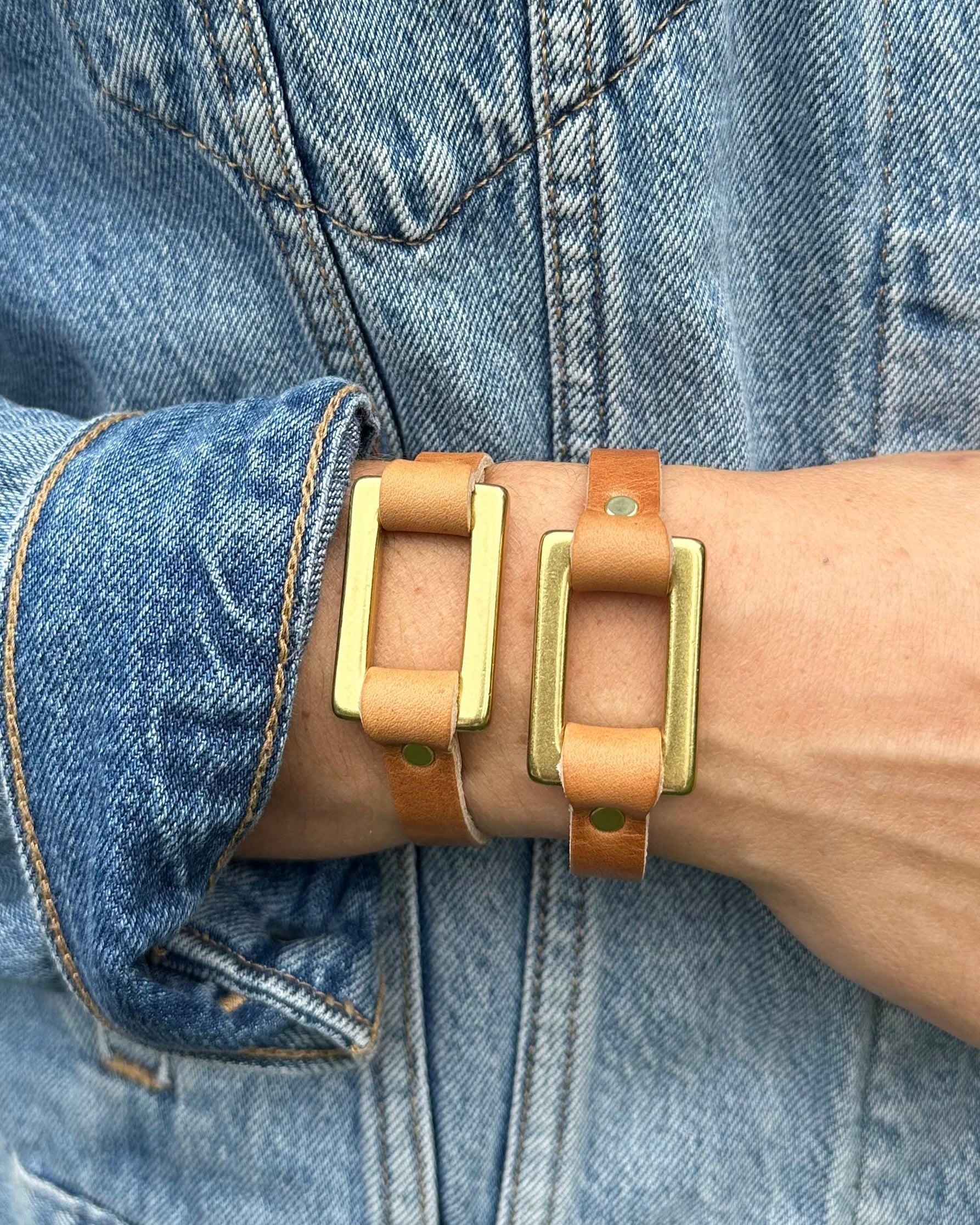 Closeup view image of model wearing two stirrup strap bracelets in sand