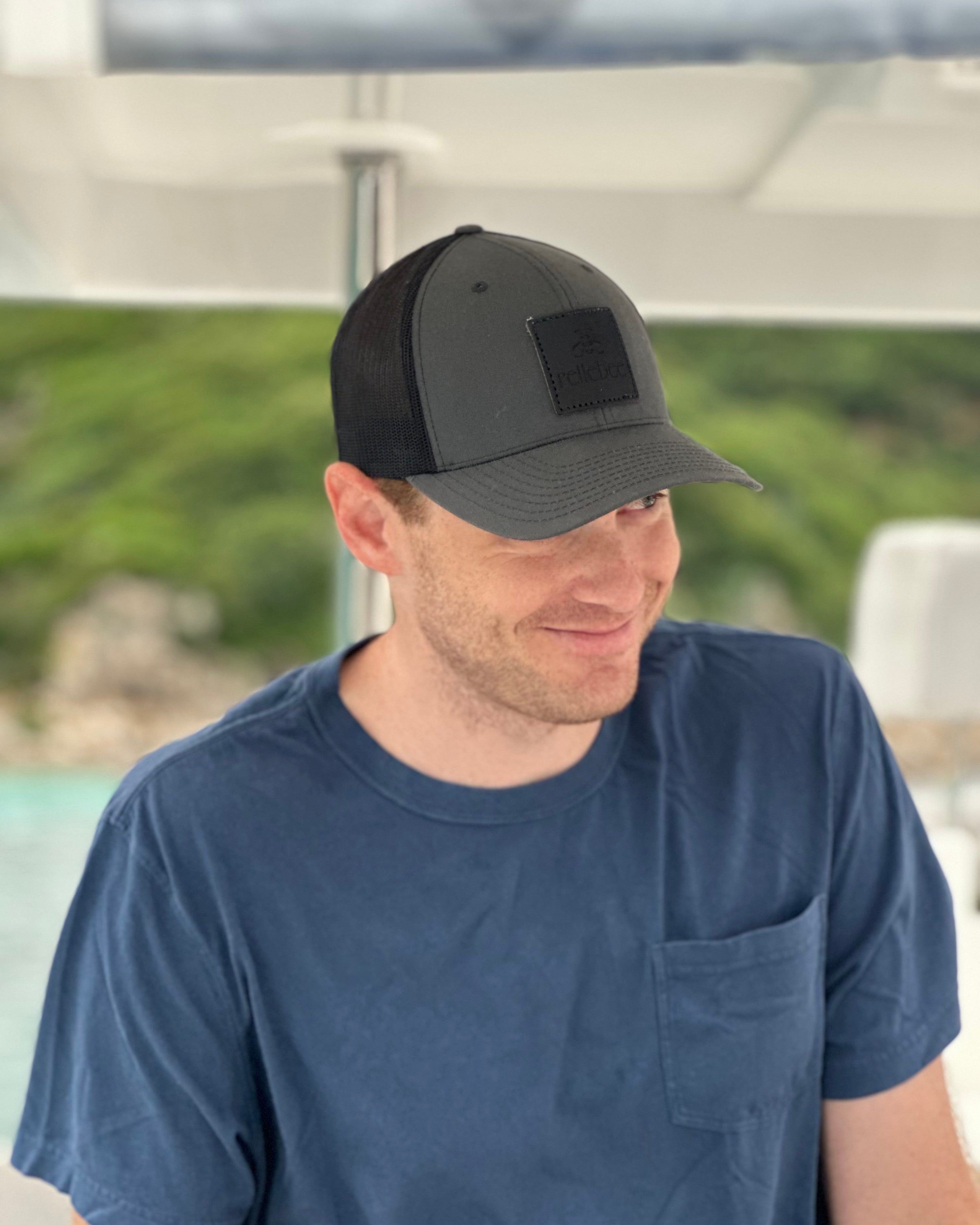 Image of model wearing the product Cap: Simple, classic, black cap with black patch. Sleek and crisp. This hat has a great fit. Adjustable.