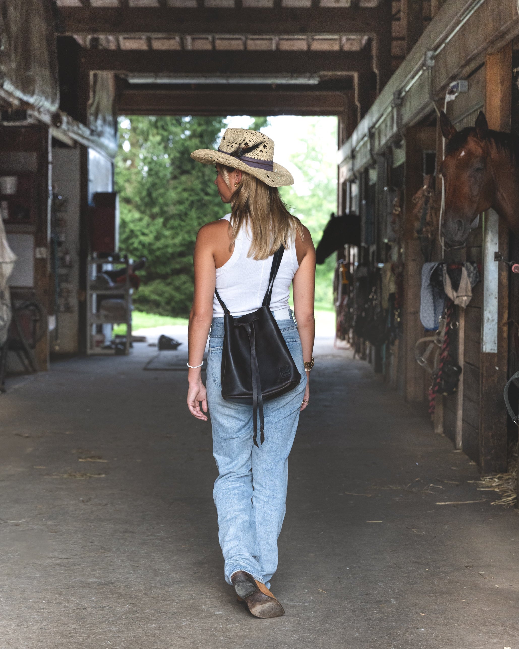 Back view image of model wearing the The Bucket Bag: Soft and buttery, slouchy with a casual feel. Easy open leather drawstring pulls it together. Nice and roomy. Big enough to hold a water bottle, clutch, phone, glasses and keys. Slip your phone into the sturdy inside pocket. Adjustable straps give you the option to wear the Bucket Bag as a cross body or over the shoulder. Easy going bag.