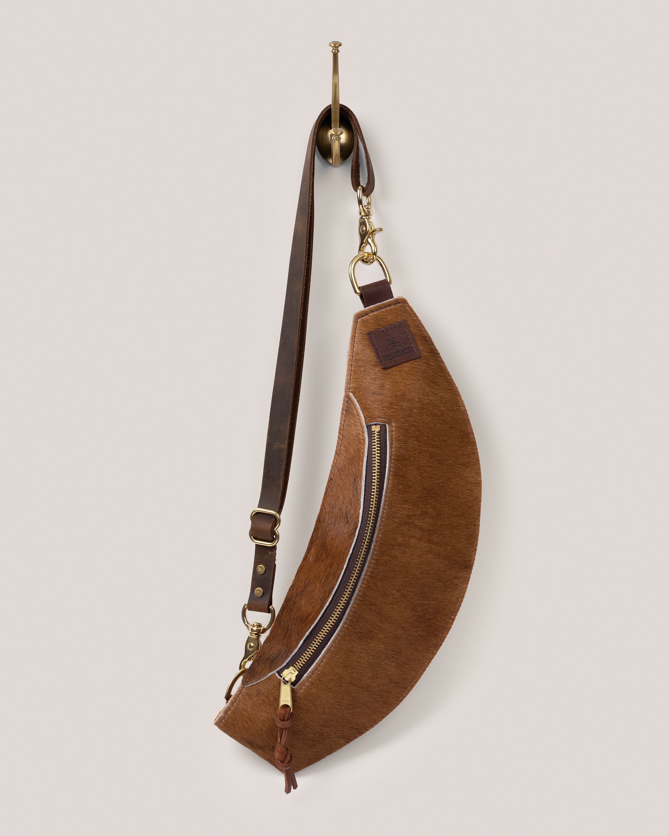 Image of the Classic Sling: Hair-on-hide in brown: low profile and gently hugs your body. Just big enough to hold your phone, keys, mini wallet and chapstick. Adjustable bridle leather straps. Sturdy top of the line antique brass hardware and zipper. This Guernsey Hair-on-Hide collection gives the Classic Sling an extra level of playfulness and fun.