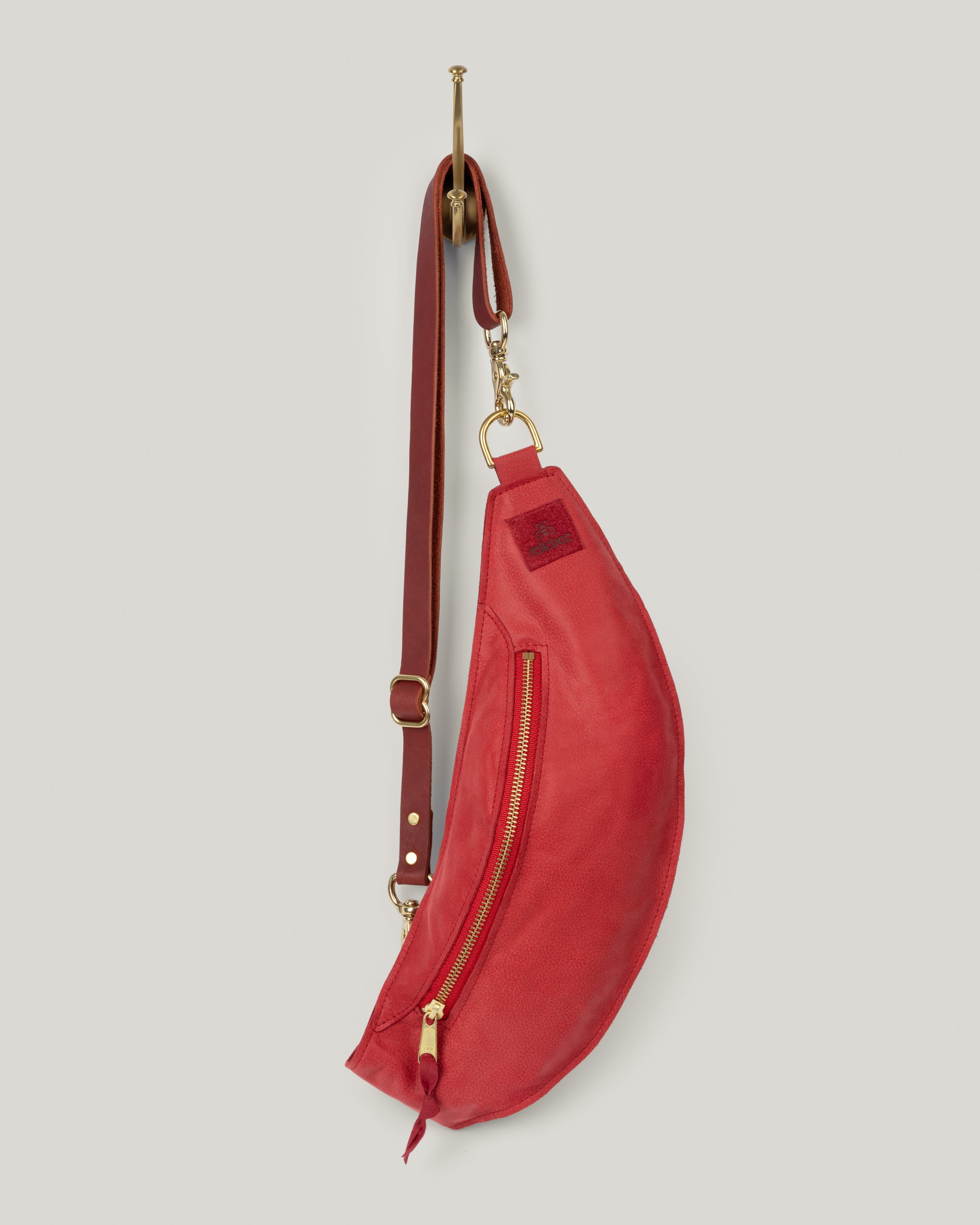 Image of product Classic sling in cherry red: The Classic Sling is low profile and gently hugs your body. Just big enough to hold your phone, keys, mini wallet and chapstick. Adjustable bridle leather straps. Sturdy top of the line antique brass hardware and zipper.