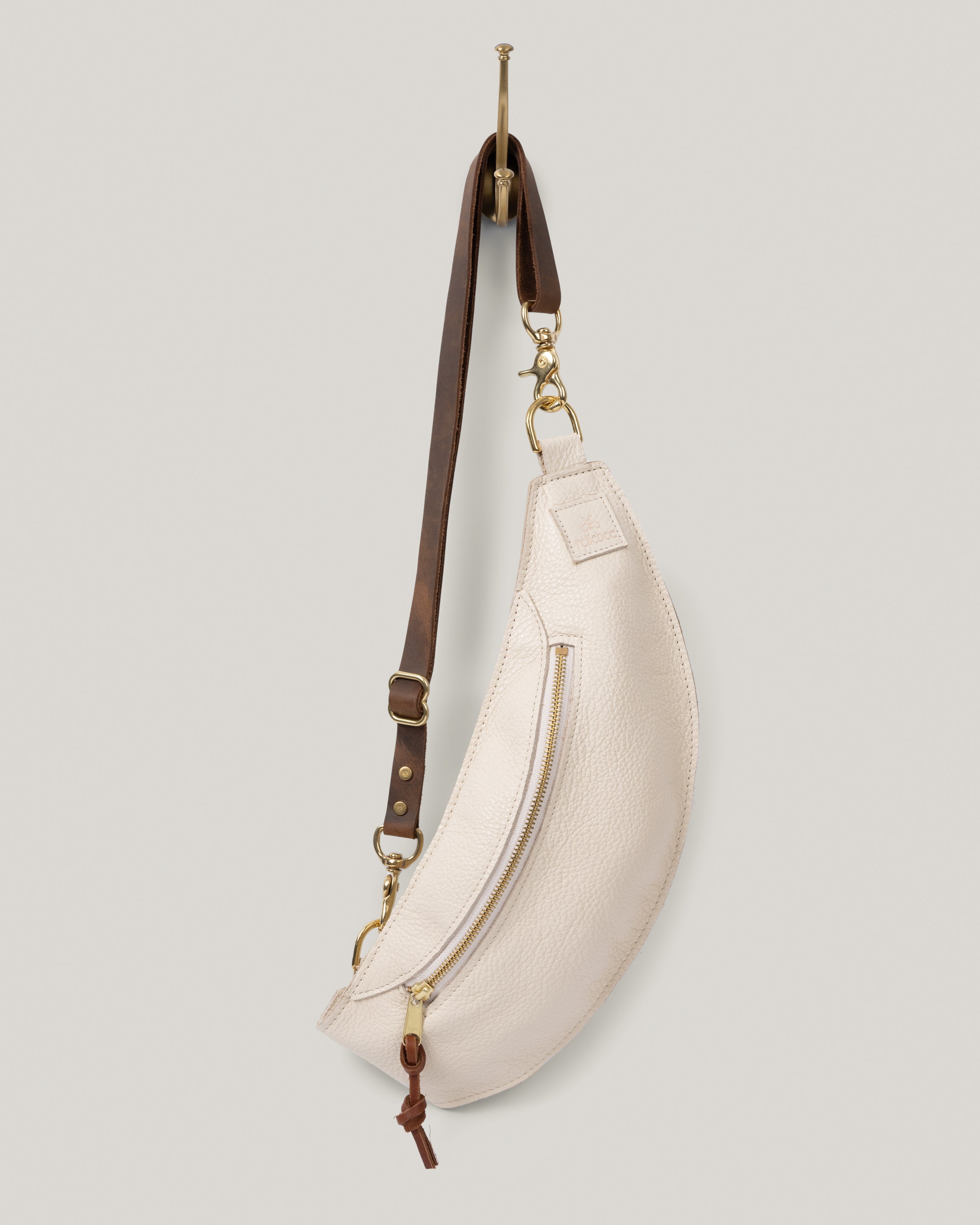Image of product Classic sling in oat milk: The Classic Sling is low profile and gently hugs your body. Just big enough to hold your phone, keys, mini wallet and chapstick. Adjustable bridle leather straps. Sturdy top of the line antique brass hardware and zipper.