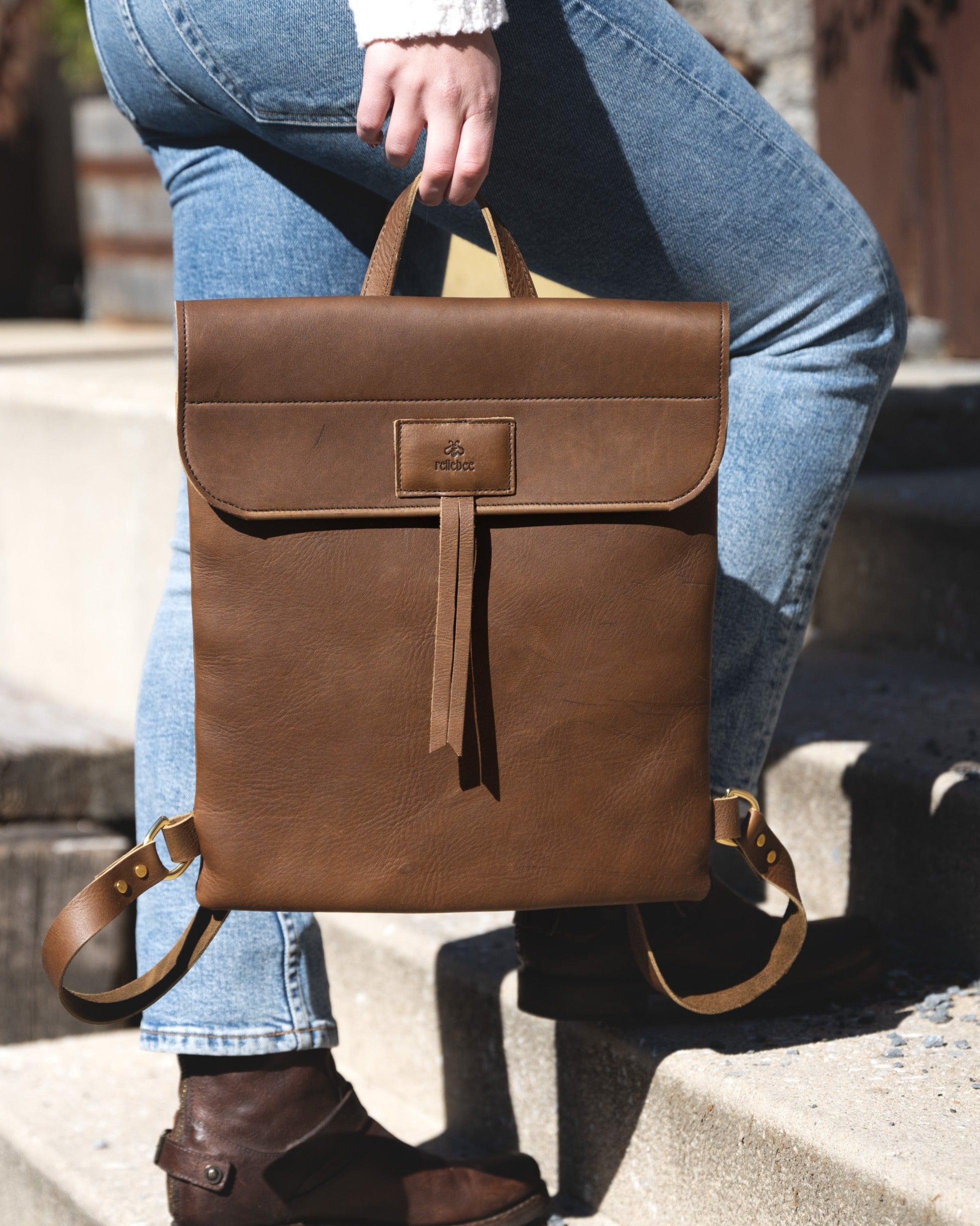 Close up image of model holding the product Messenger pack in Olive Brown: The perfect go to bag for your laptop, notebook, folder, clutch and other items. Inside pocket. Strong magnetic closure. The two leather strips function well for easy access and a pop of personality. Made up in a sturdy Olive Brown and a Jet Black hide from Wisconsin. Black topstitching. This bag is sleek and sophisticated. It will take you through any important meeting or wherever adventure leads you.