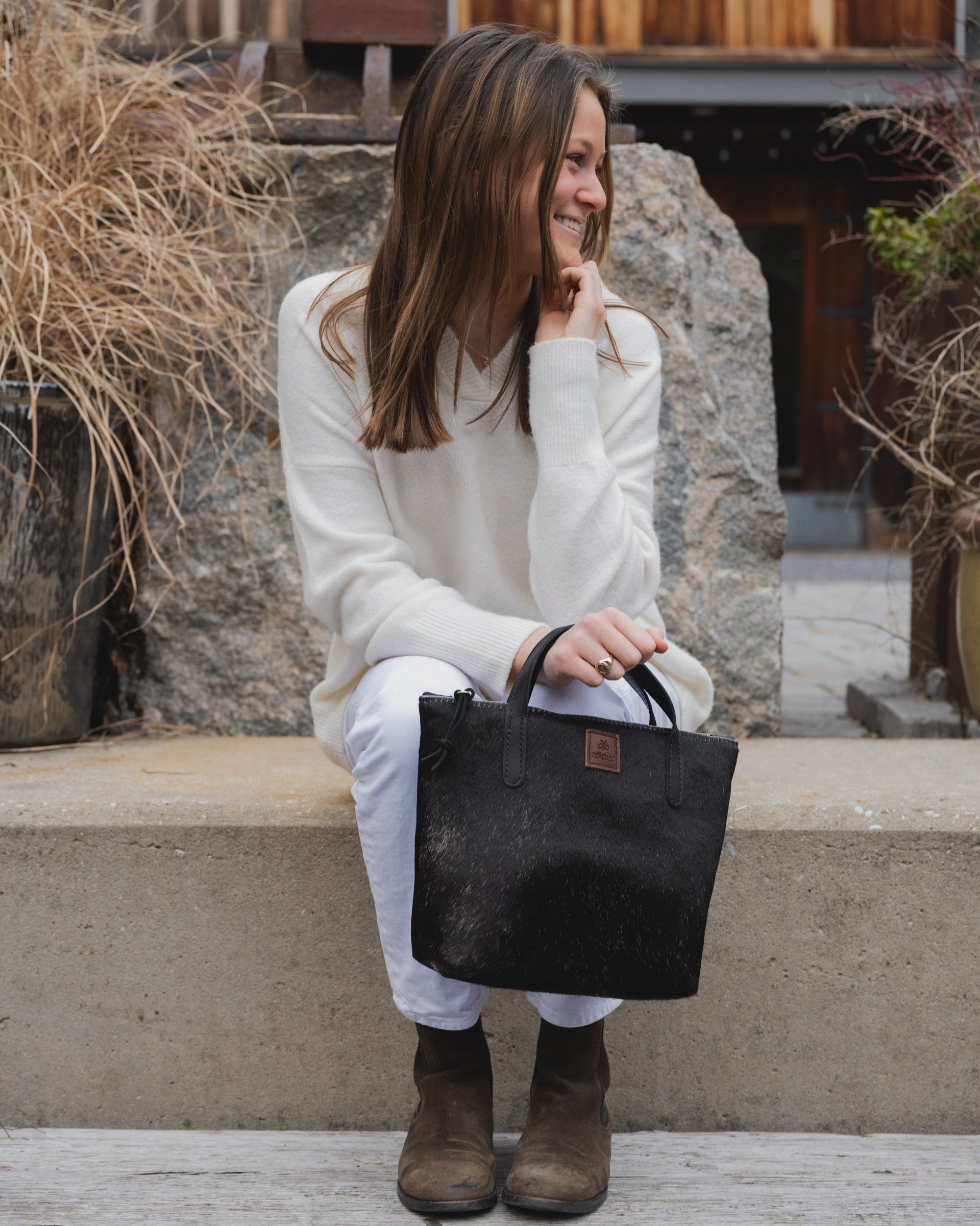 Image of model holding The Tuscan tote in black. The Tuscan tote with the sturdy brass zipper is the perfect bag to carry your water bottle, keys, wallet, phone and a clutch. Inside pocket. Light in weight. It's a fun easy shape with a casual mountain feel.